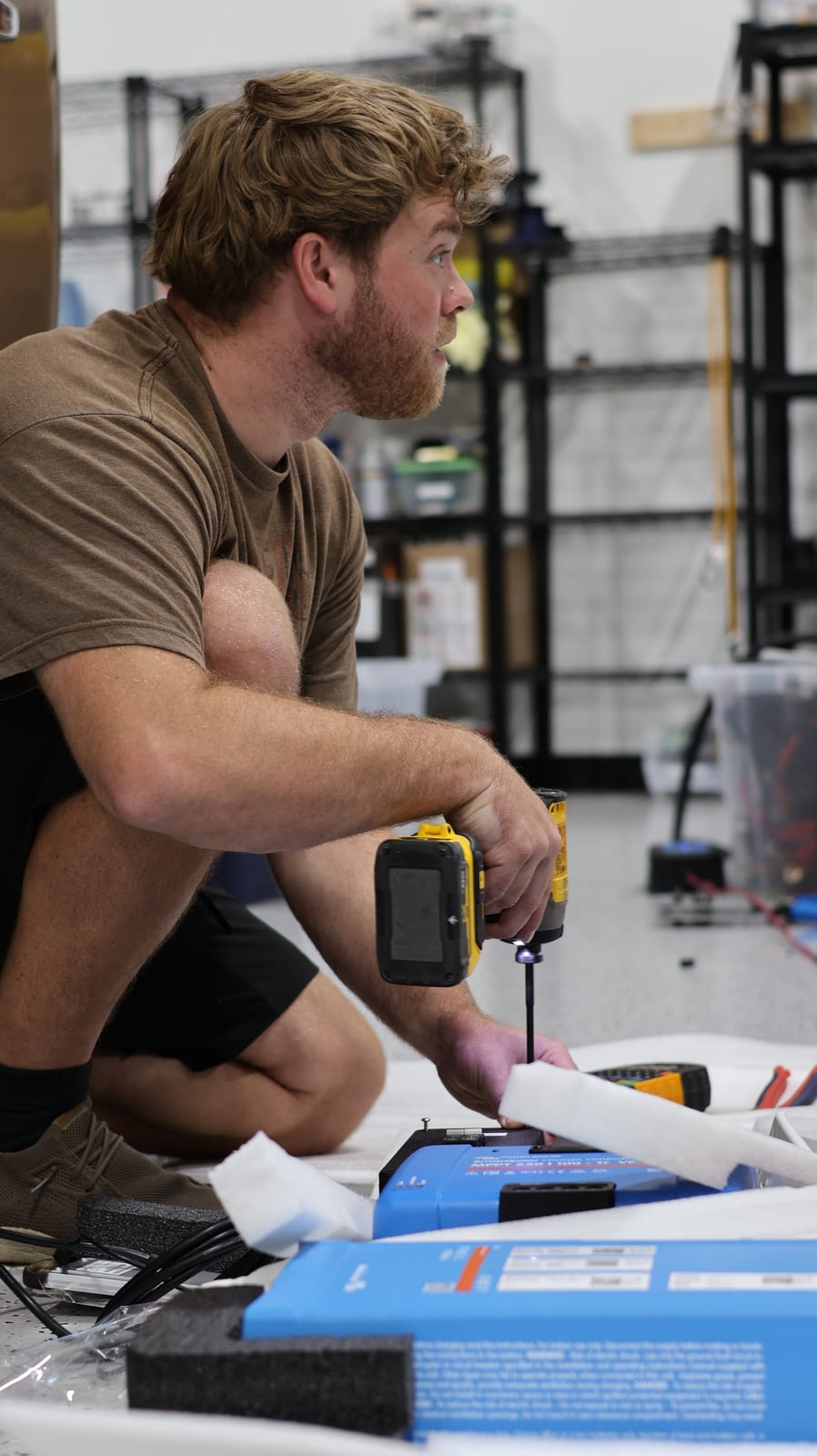 Technician kneeling at a workbench with a multimeter, testing components