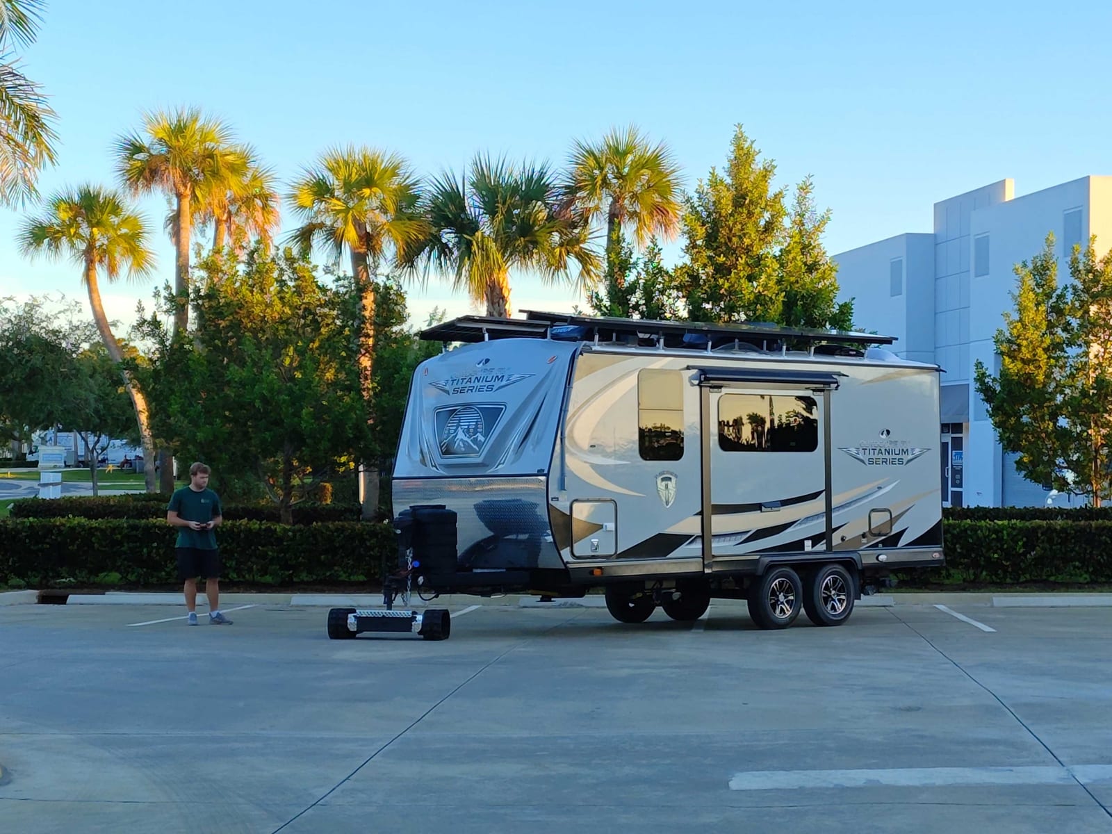 Travel trailer with rooftop solar panels parked outside the shop among palm trees